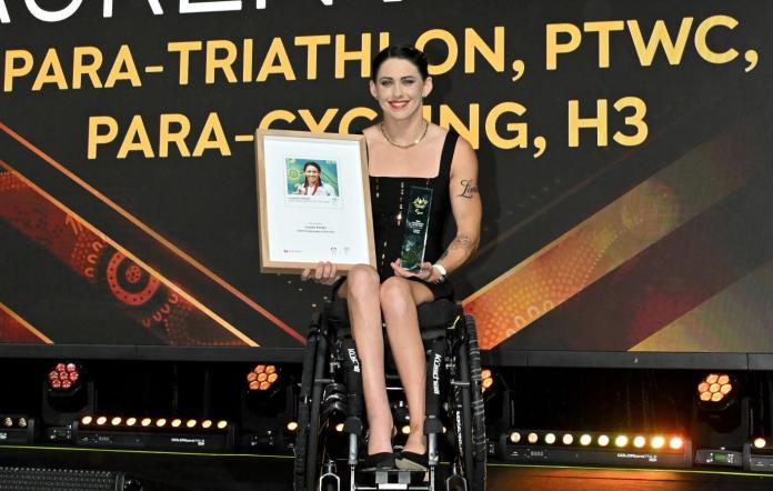 A female Para athlete is on a stage holding a frame with a photograph of herself