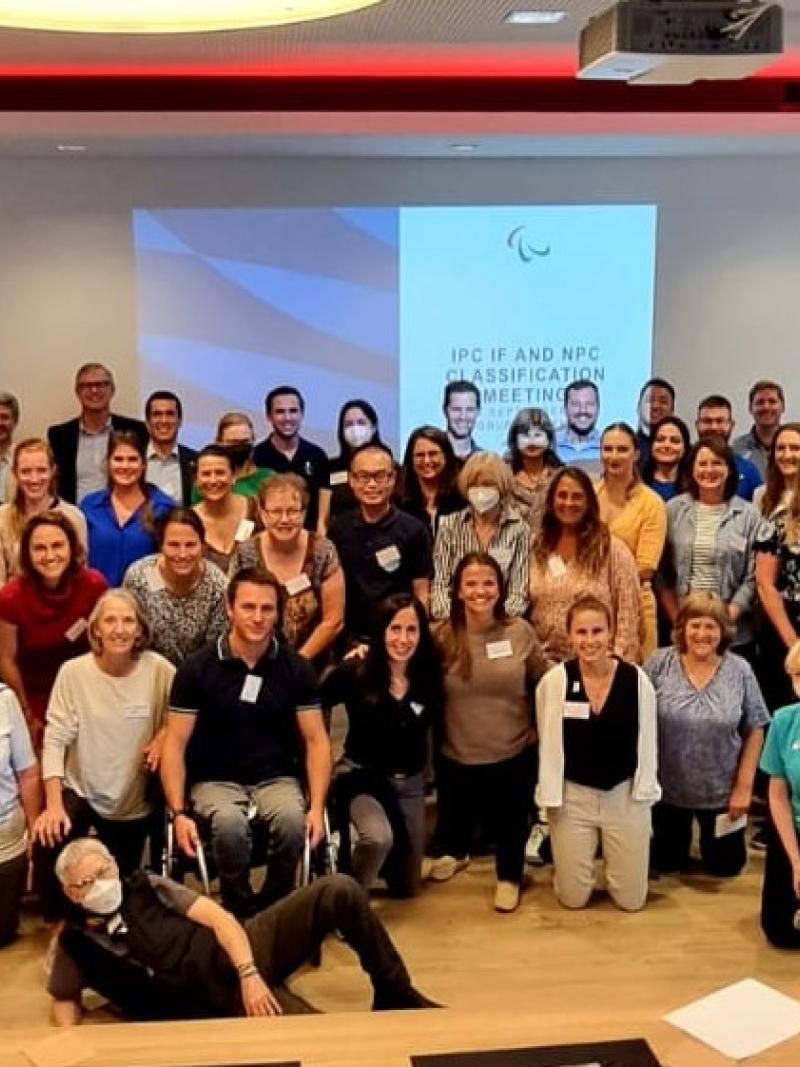 More than 70 people pose for a group photo in front of a screen that says "IPC IF and NPC Classification Meeting"