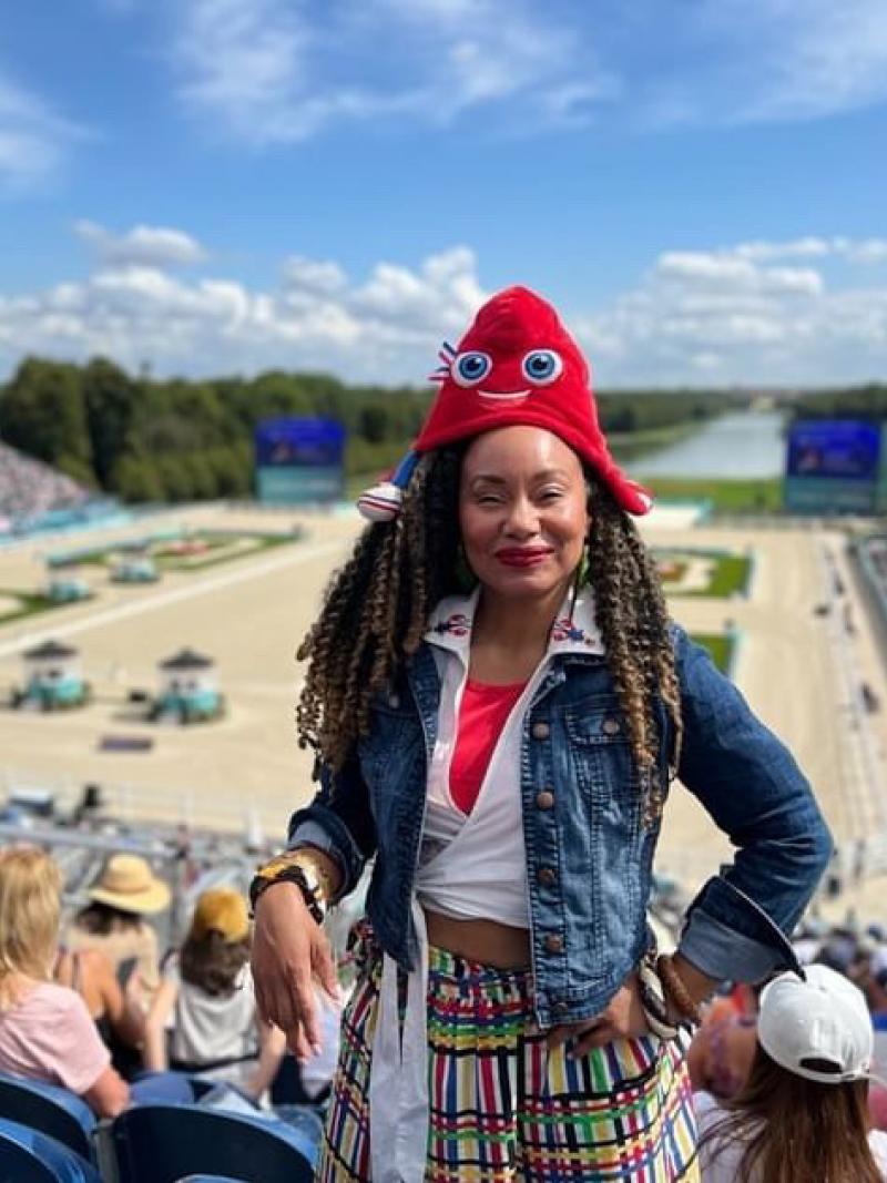 Woman stands facing camera with backdrop of Chateau Versailles Para equestrian wearing Phryge mascot hat