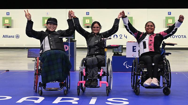 Three women in wheelchairs holding hands in a shooting range
