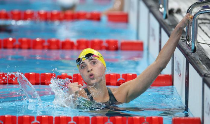 A female Para swimmer pumps her fist in the pool after finishing a race