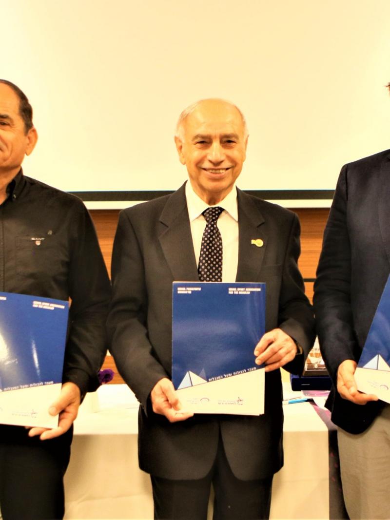 Three men in suits smiling holding a folder