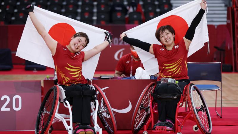 Sarina Satomi and Yuma Yamazaki are smiling as they sit and hold the Japanese flags after winning gold at Tokyo 2020