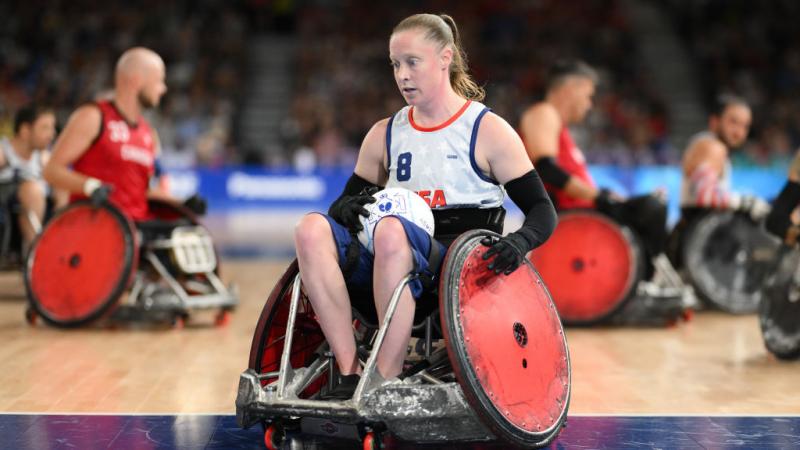 Woman in a white USA tea in wheelchair with red wheels holding a rugby ball