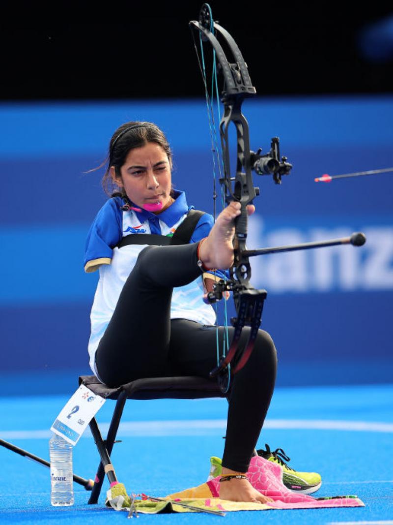 A woman shoots an arrow, holding the bow with her foot