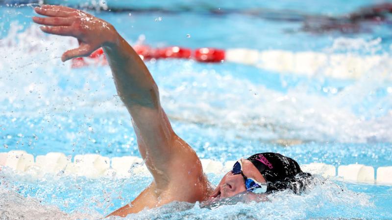A man swimming reaches an arm out of the water and tilts his head up to take a breath