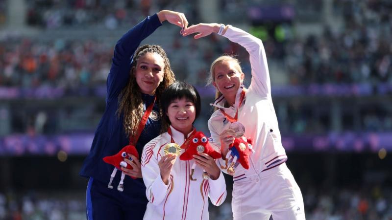 Three women on a podium celebrating their medals