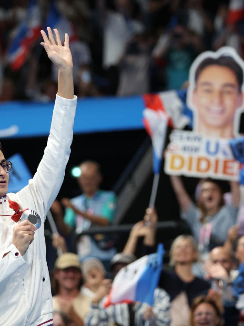 A young man with a medal waving to the crowd in an indoor arena