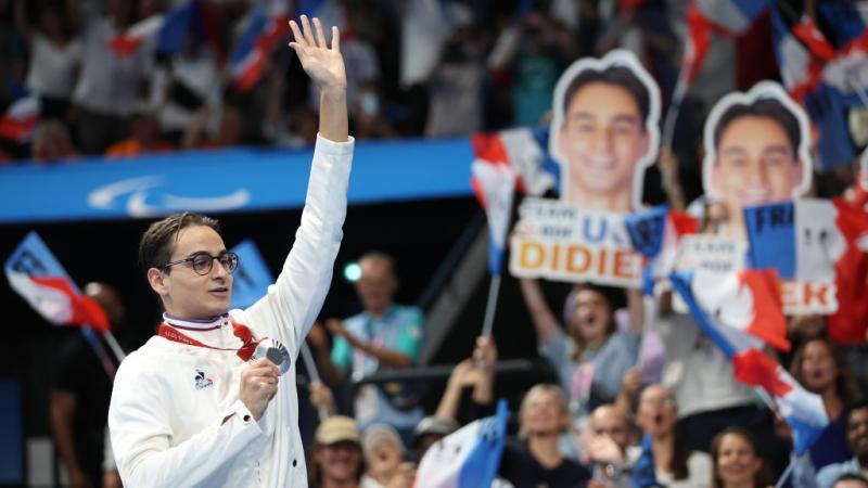 A young man with a medal waving to the crowd in an indoor arena