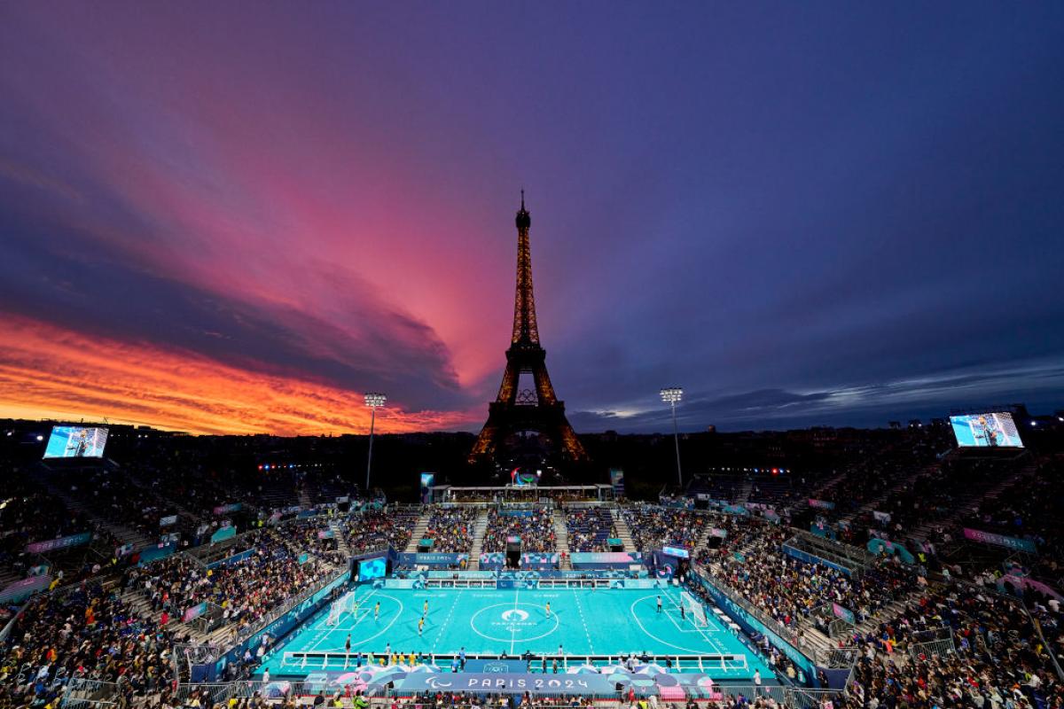 A view of the outdoor Paris 2024 blind football stadium at sunset, with the Eiffel Tower in the background