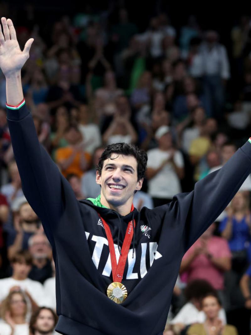 A man in a Team Italy sweater wearing a gold medal raises his arms in the air in celebration in front of a crowd of people at La Defense Arena