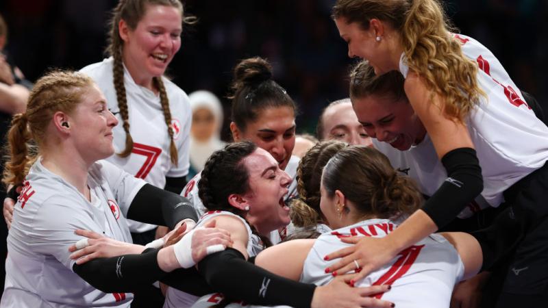 Canada's women's sitting volleyball team put their arms around each other and cheer in celebration