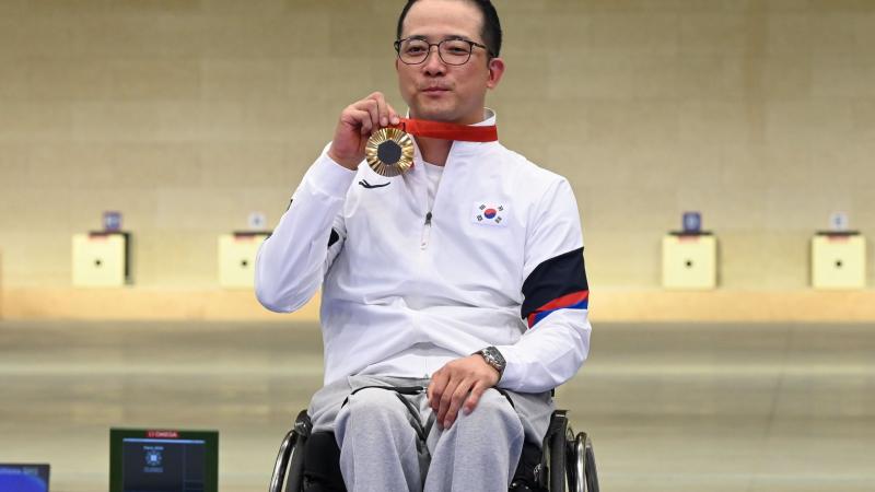 A man in a wheelchair showing his gold medal in a shooting range