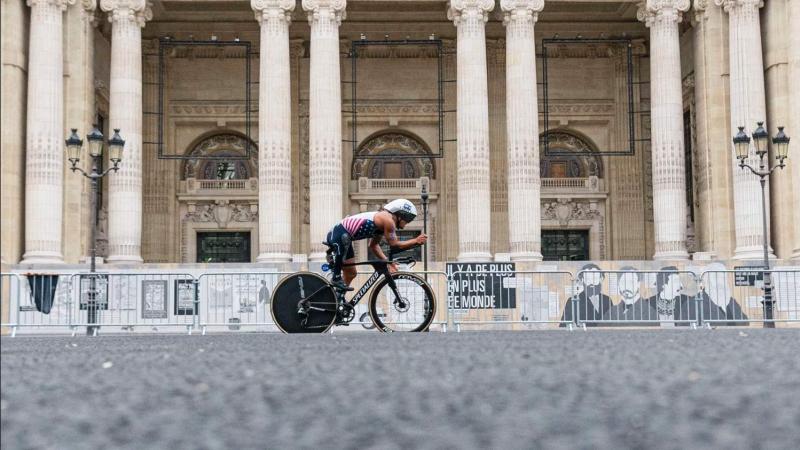 A Para triathlete on a bike cycles past a Parisian monument 