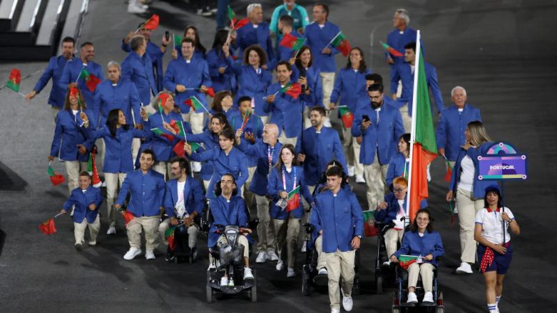 About 30 athletes take part in the parade of nations at the Paris 2024 Paralympic Opening Ceremony. They are all wearing a blue jacket and carries small flags of Portugal