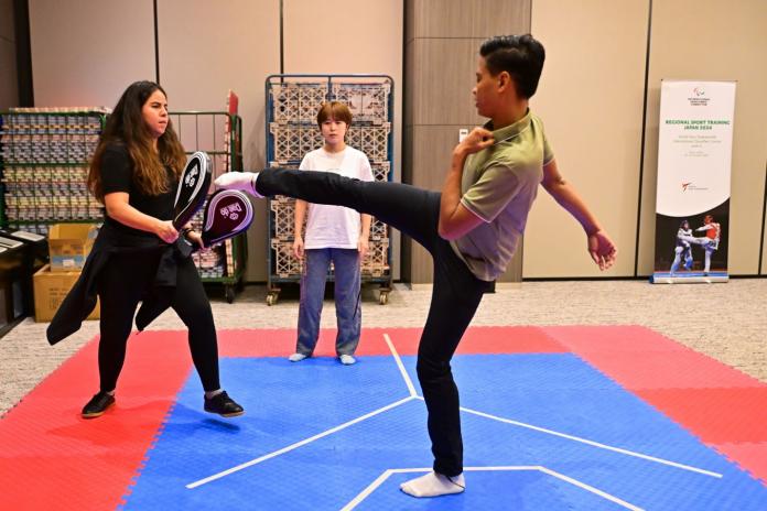 A man is demonstrating a taekwondo kick on a red and blue mat