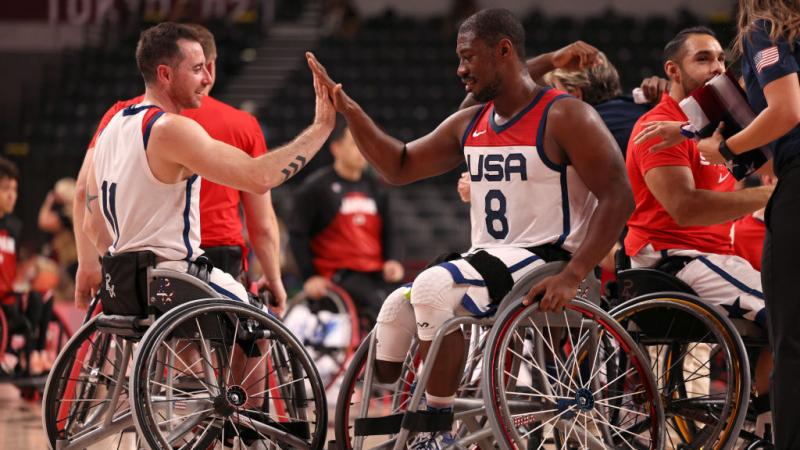 Two male wheelchair basketball players do a high-five to celebrate a victory