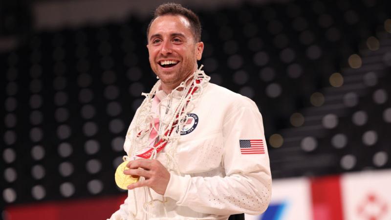 A male wheelchair basketball player posing for a photo while holding a gold medal. 