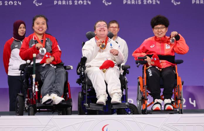 Three boccia athletes - Aurelie Aubert of Team France (C), Silver medalist Yee Ting Jeralyn Tan of Team Singapore (L) and Bronze medalist Hiromi Endo of Team Japan (R)  - are holding their medals on a white podium