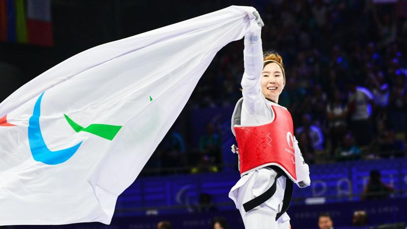 Zakia Khudadadi, a female Para taekwondo athlete, runs while holding the Paralympic flag with her right hand